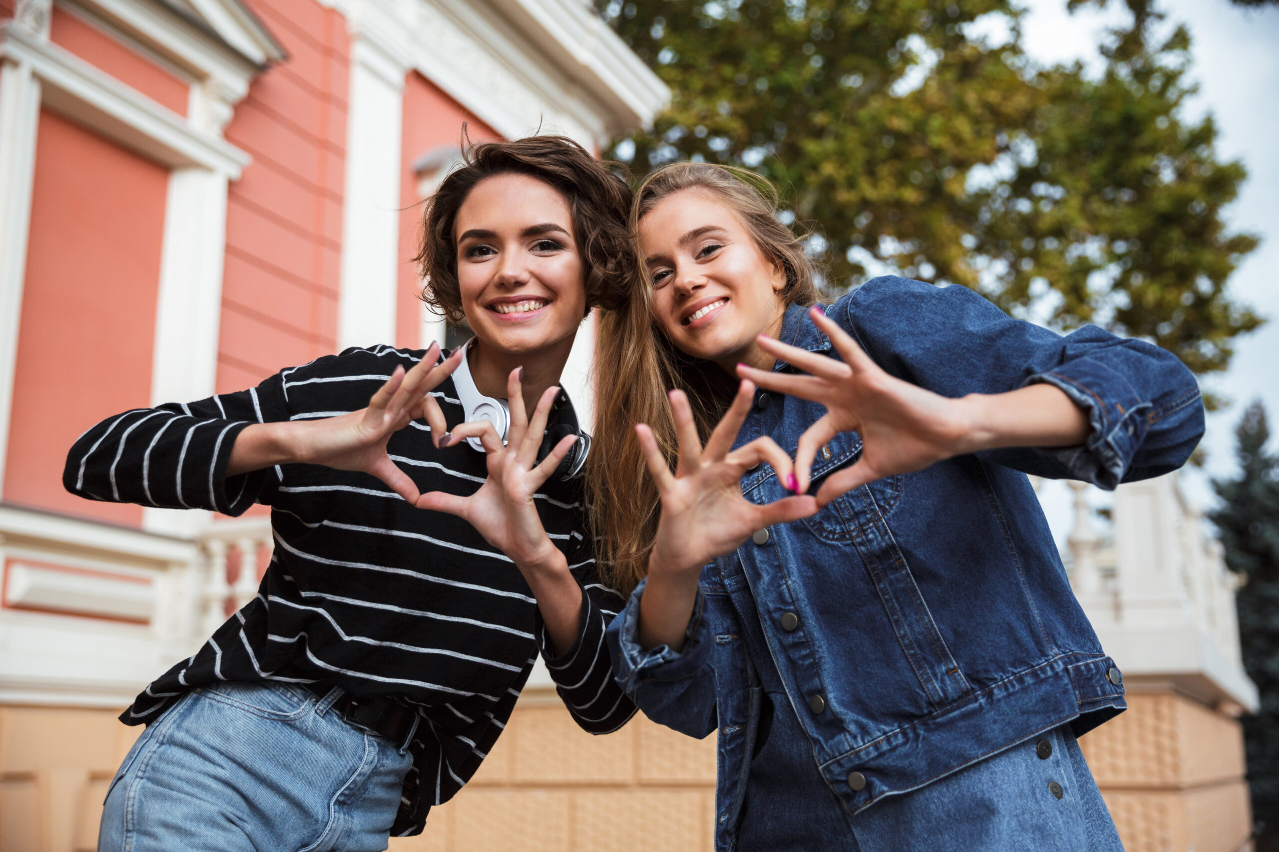 Two smiling happy teenage girls showing love gesture