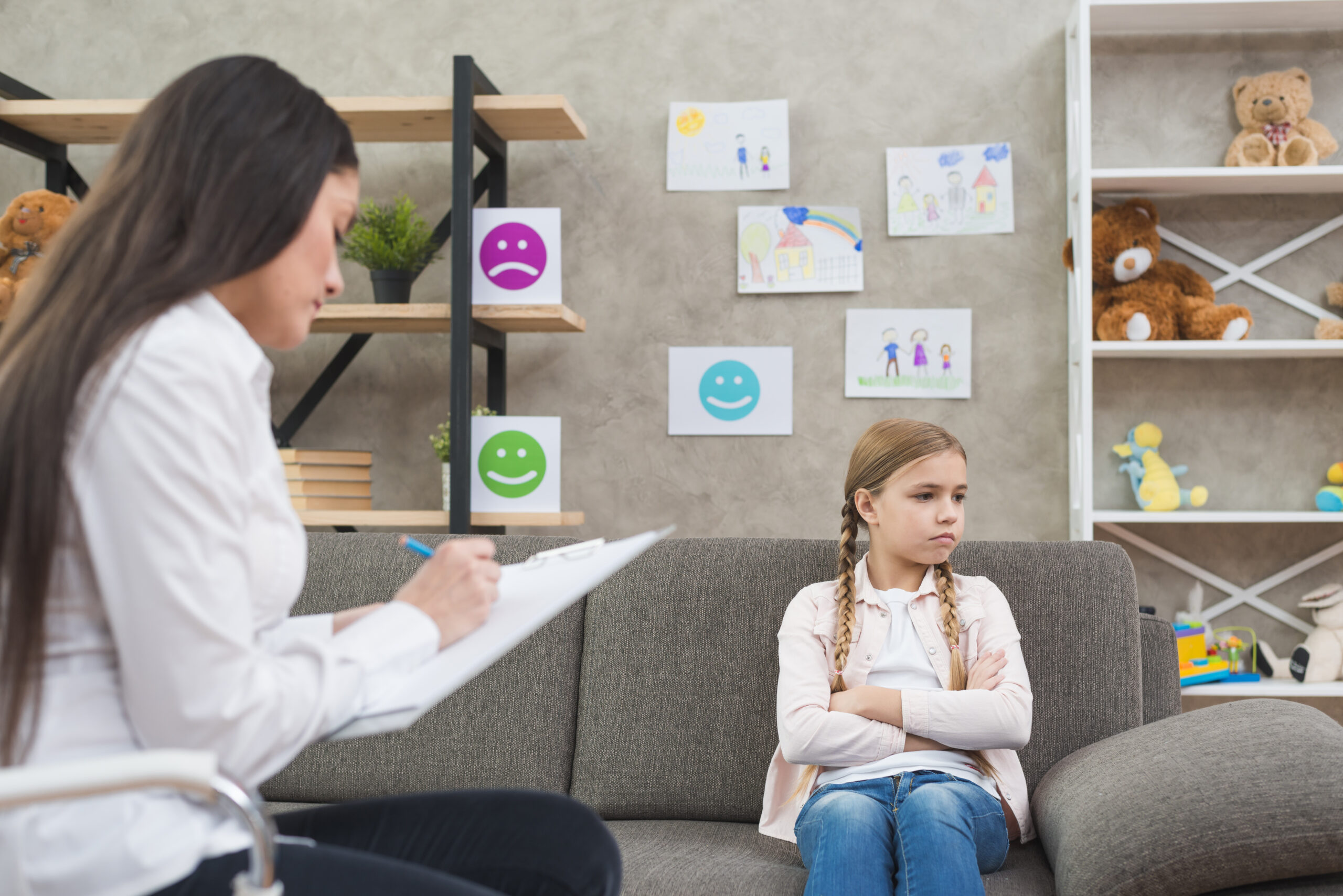 depressed-girl-sitting-sofa-with-female-psychologist-writing-note-clipboard