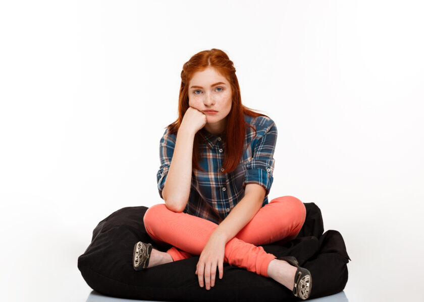 Portrait of beautiful ginger girl sitting crosslegged over white background.