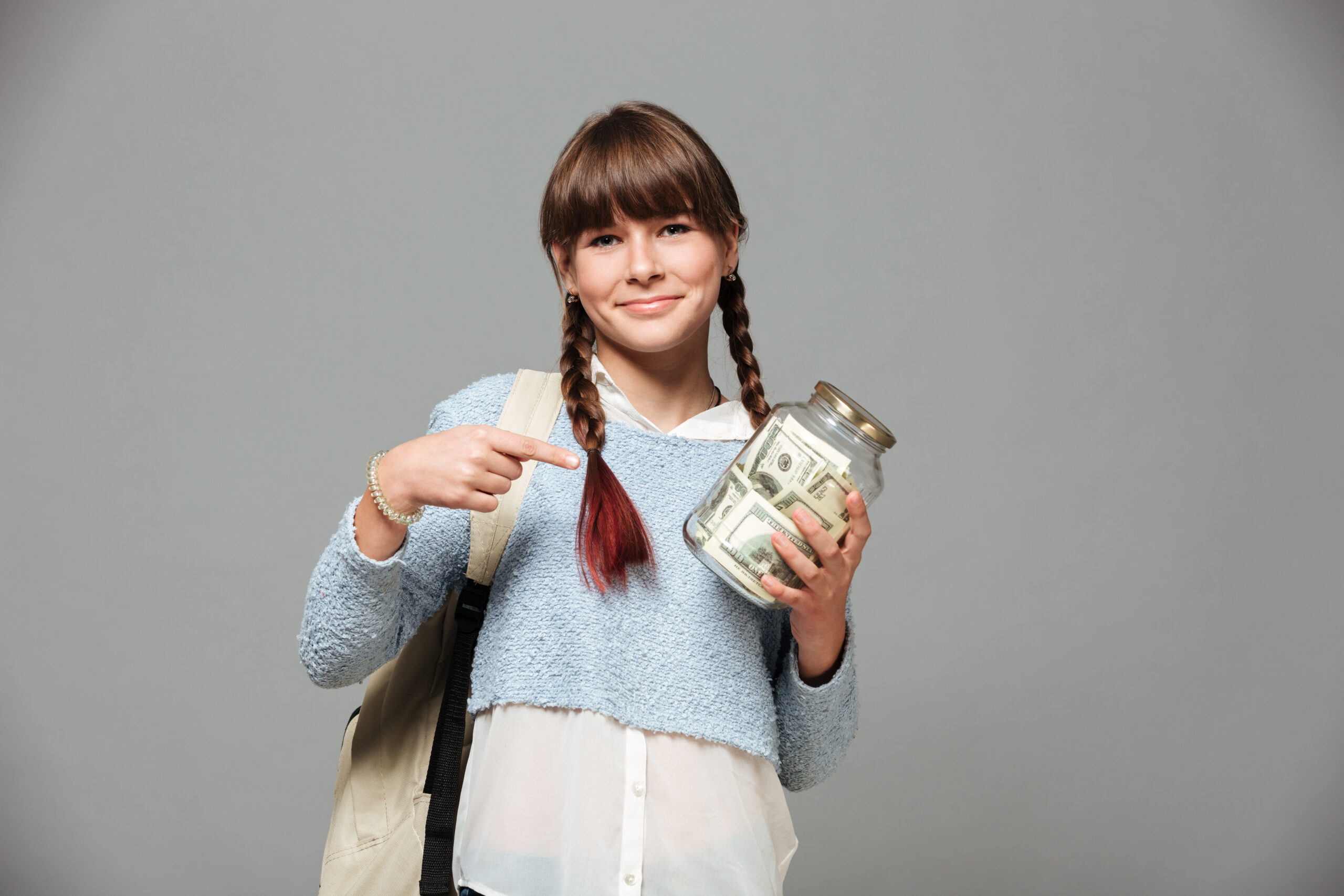 Girl standing isolated grey background with jar full of money