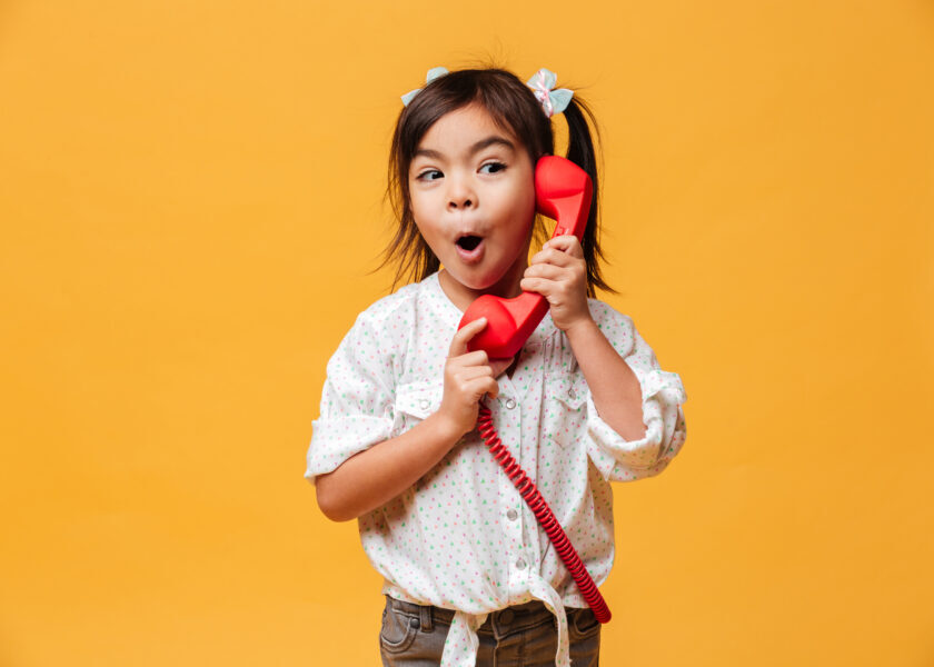 Shocked excited little girl talking by red retro telephone.