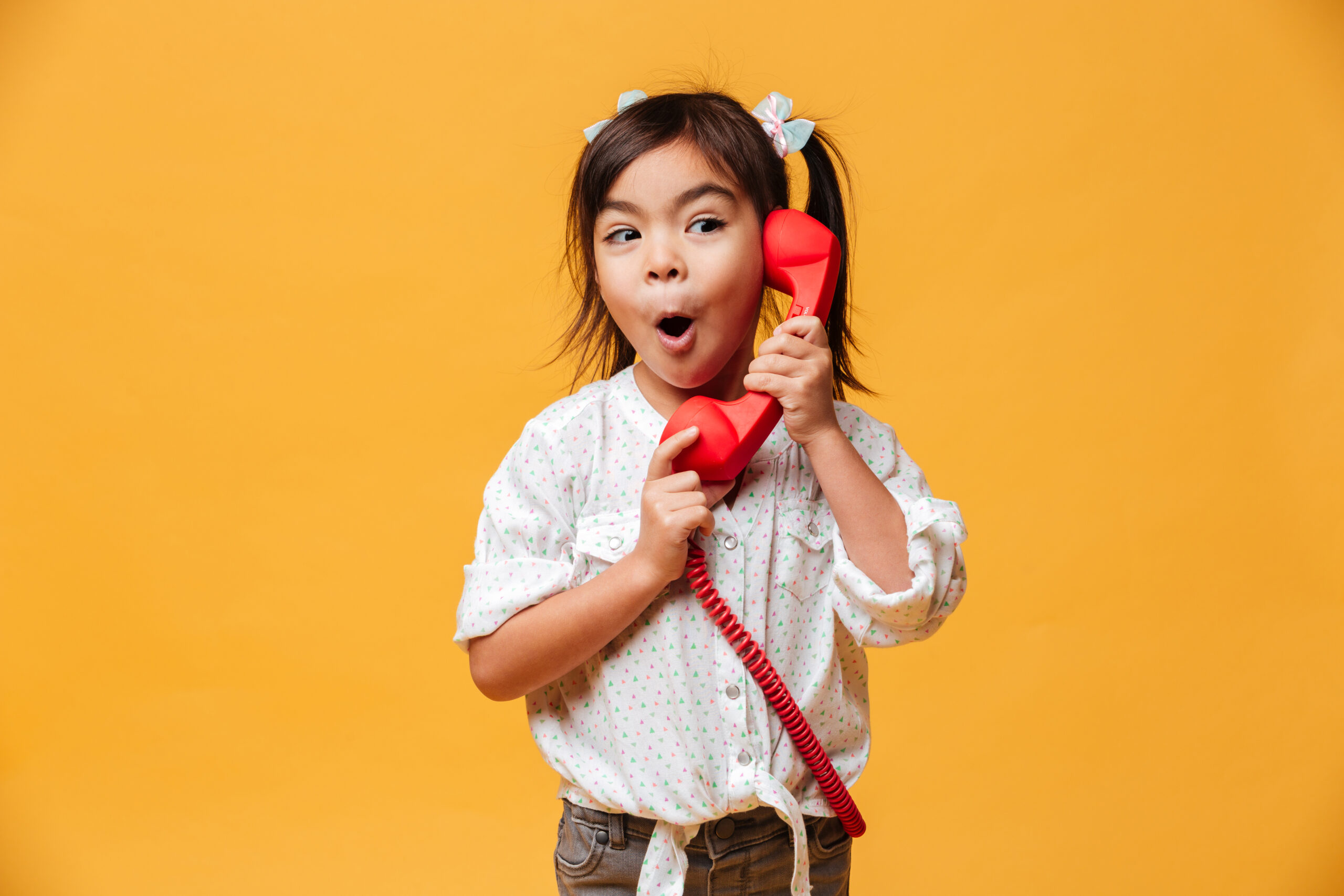 Shocked excited little girl talking by red retro telephone.