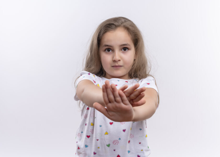 looking at camera little school girl wearing white t-shirt showing stop gesture on isolated white background